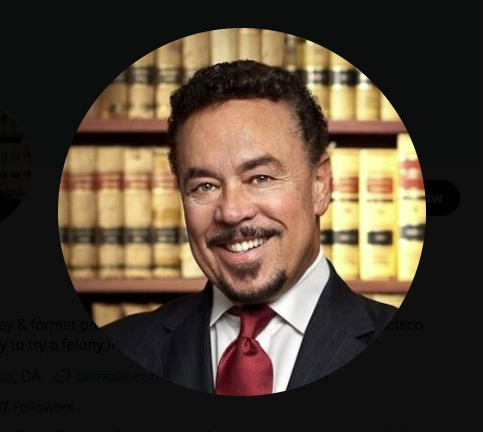Antonio Malik Rodgers-Alcala, a man in a suit and tie, is smiling in front of a bookshelf.