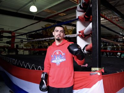 Carlos Aroche in a red shirt standing in front of a boxing ring.