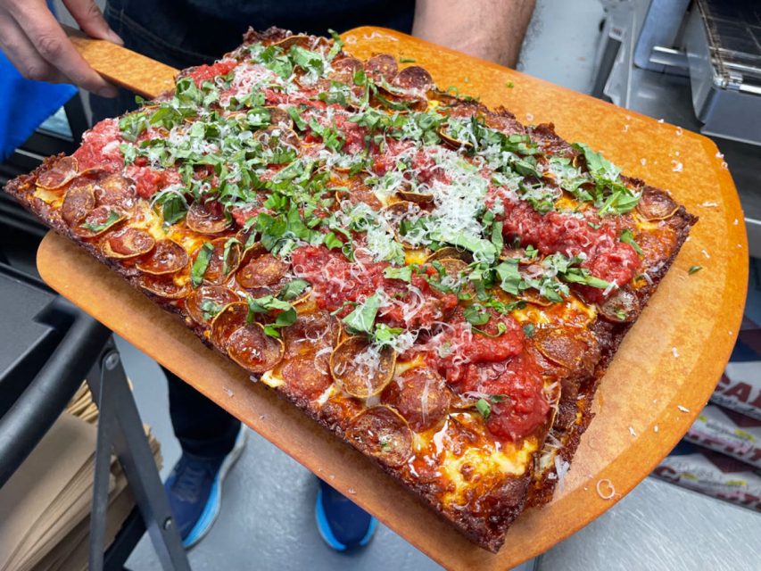 A person is holding a large pizza on a wooden board.