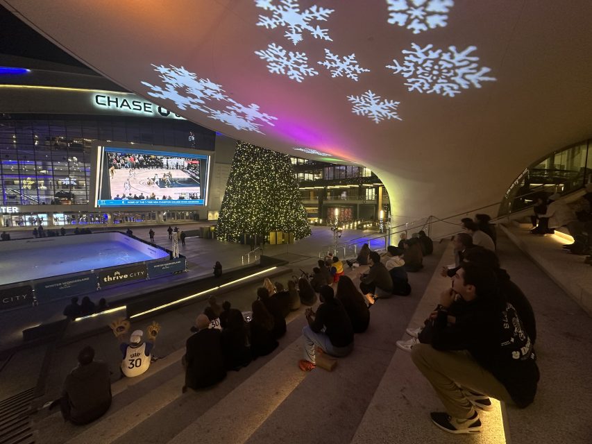 A group of people are sitting on steps watching a projection of snowflakes.