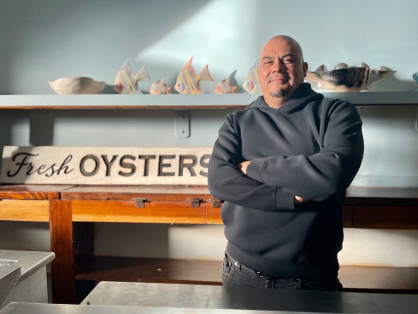 A man standing in front of a sign that says fresh oysters.