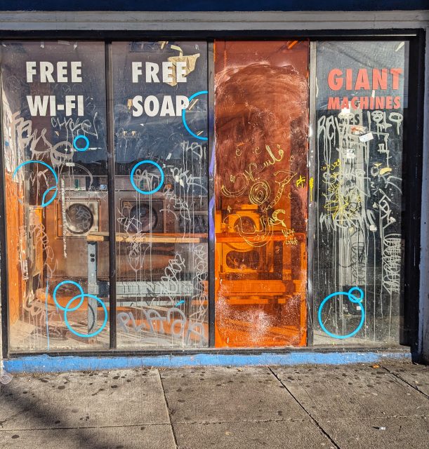 A storefront with graffiti-covered windows advertising "free wi-fi," "free soap," and "giant machines.