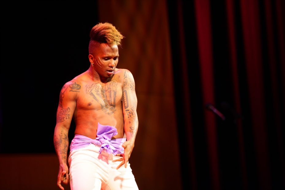 Shirtless performer with tattoos on a stage.