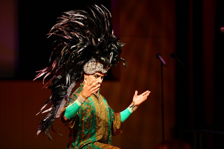 Performer in an elaborate costume and headdress on stage.