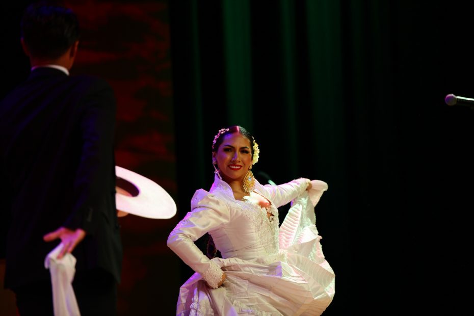 Woman in white dress performing traditional dance on stage. She competes to rule Carnaval.