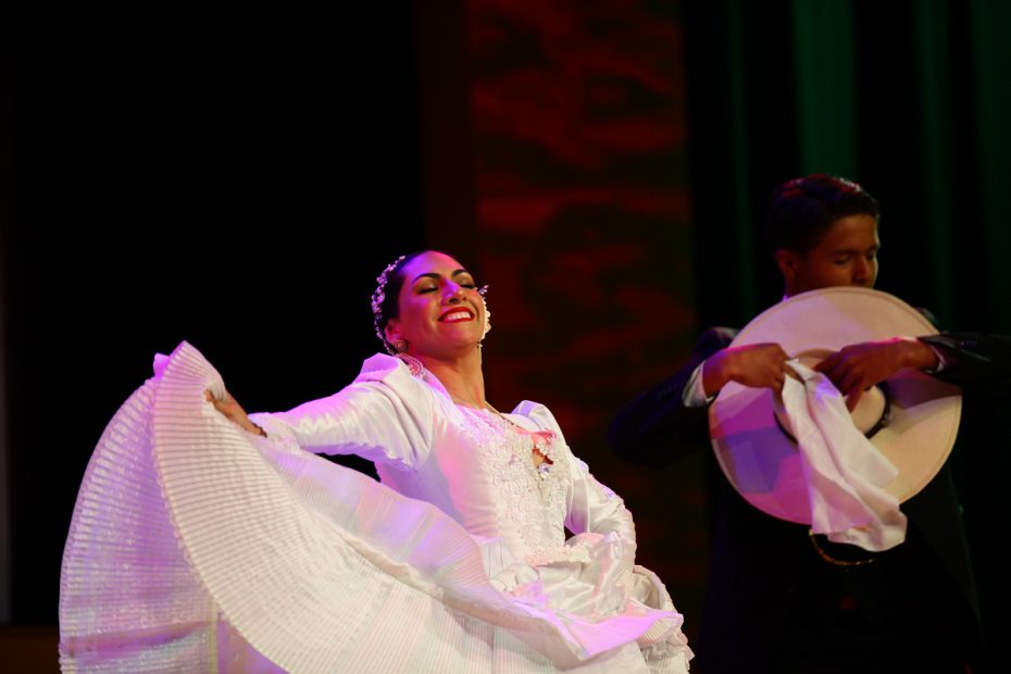 Traditional dancers performing with white handkerchiefs on stage. She competes to rule Carnaval.