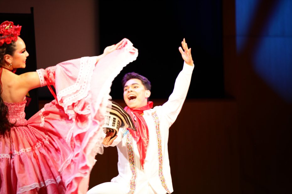 A male and female dancer in traditional vibrant costumes performing onstage.
