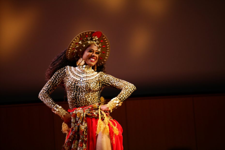 A performer in traditional indian dance attire smiling on stage. She is competing to rule Carnaval.