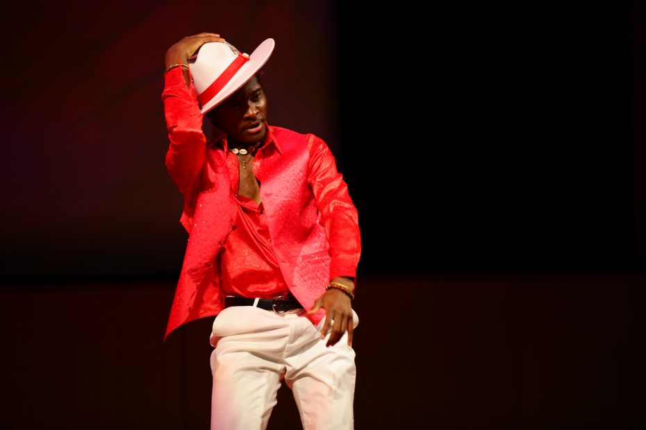 Performer in a red sequined jacket and white hat striking a pose on stage.