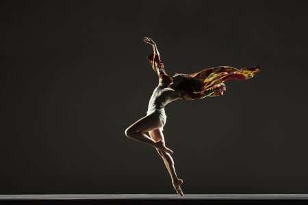 Alonzo King LINES Ballet's Ilaria Guerra captured mid-twirl, with a colorful shawl flowing behind her against a dark background.