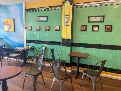 Interior of a coffee shop with empty tables, metal chairs, and decorative wall art.
