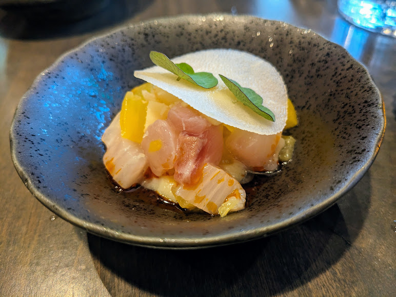A gourmet dish of diced raw fish topped with a foam and garnished with a green leaf, served in a dark bowl at Foliage.