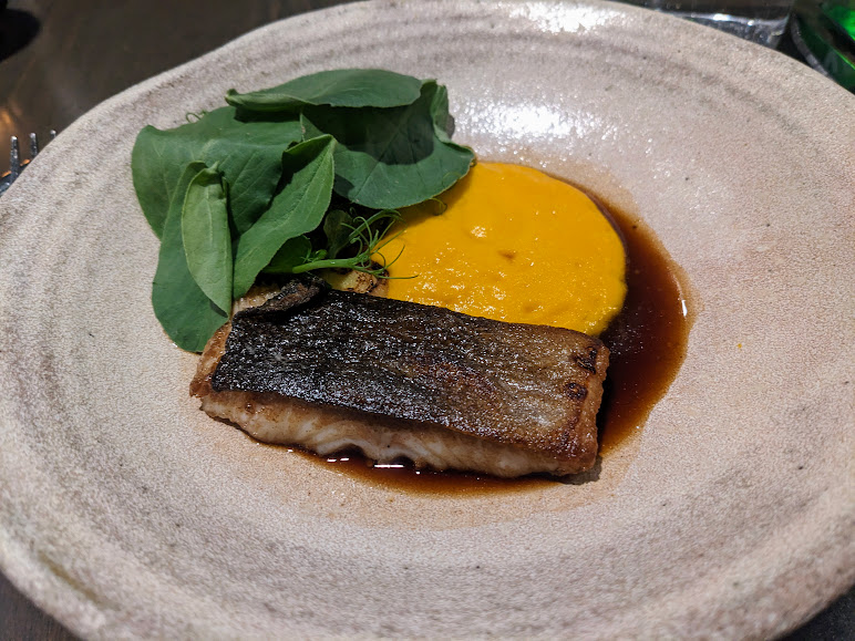 Pan-seared fish fillet with a pureed sauce and fresh greens on a ceramic plate.