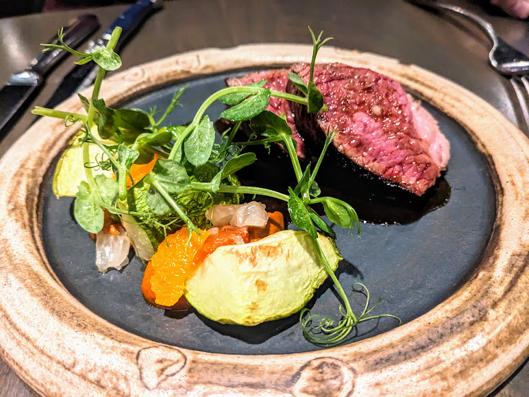 Grilled steak served with fresh greens and citrus fruit on a rustic plate.