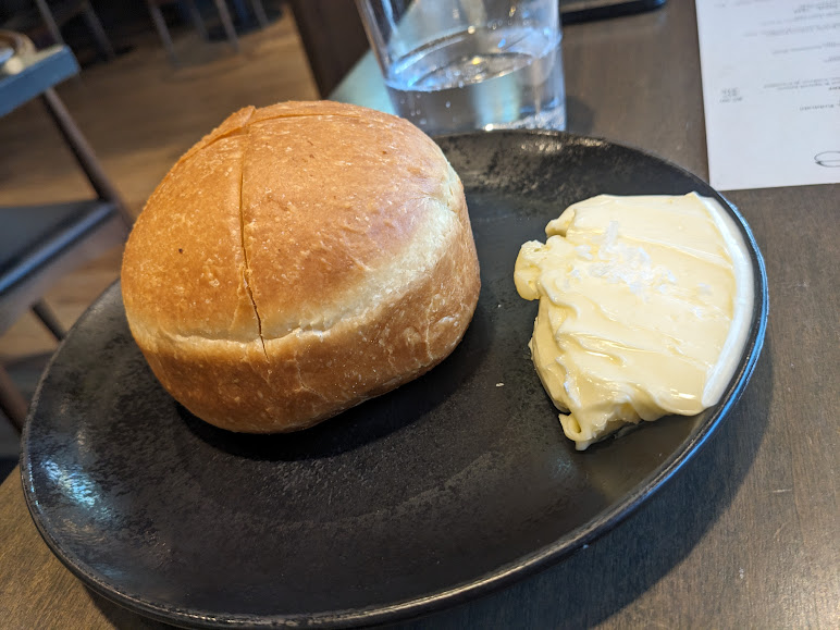 A fresh bread roll served with a pat of butter on a black plate at Foliage.