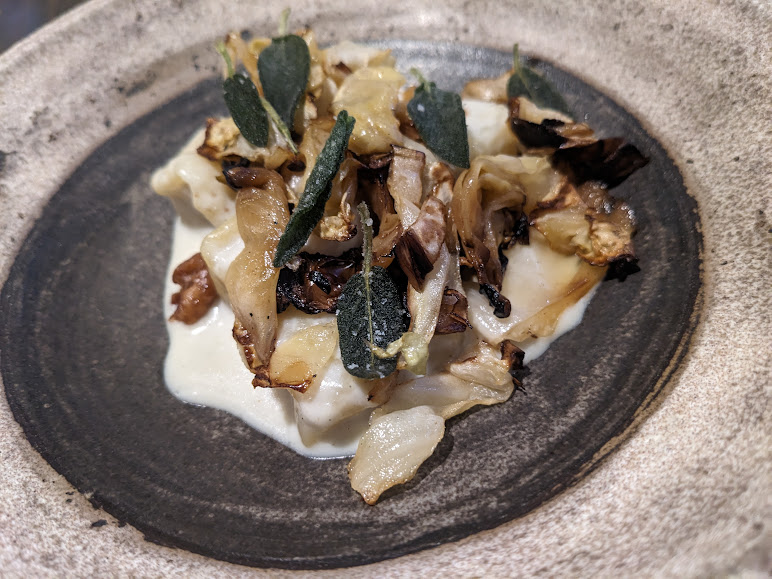 Gourmet pasta dish with sautéed mushrooms and sage leaves served on a ceramic plate.