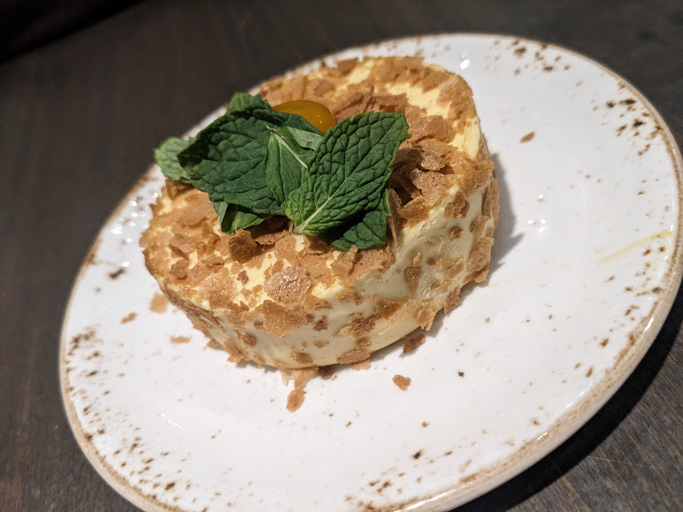 A tiramisu dessert garnished with a mint leaf and a small piece of physalis on a white plate.