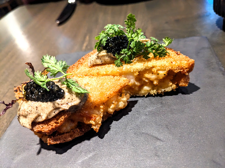Gourmet dish featuring crispy breaded food topped with a dollop of black caviar and garnished with fresh herbs, presented on a slate plate at Foliage.