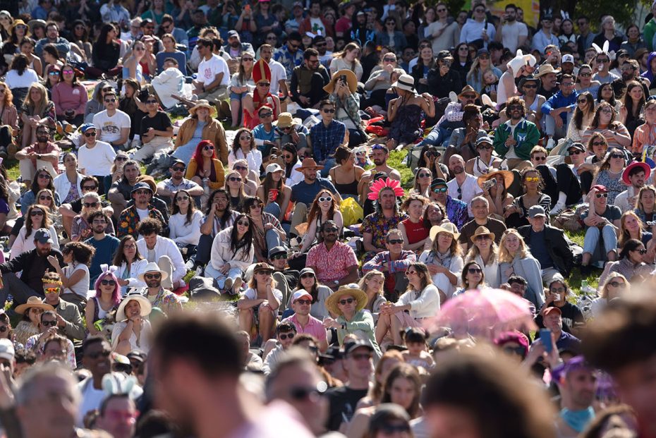 A diverse crowd of spectators at an outdoor event, many wearing hats and sunglasses.
