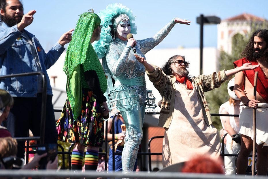 Performers in eclectic costumes engaging with each other on an outdoor stage at Hunky Jesus.