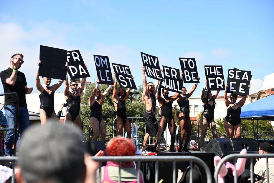 Group of people holding up lettered signs to form a message while standing on stage at an outdoor event.