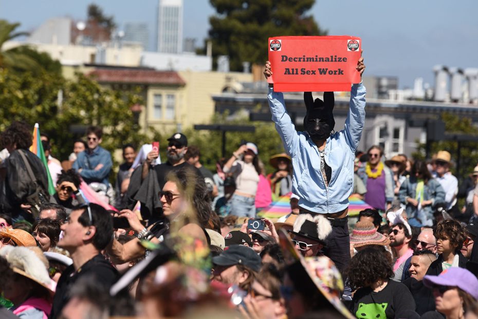 Person in a rabbit mask holding a sign advocating for the decriminalization of all sex work at a public gathering.