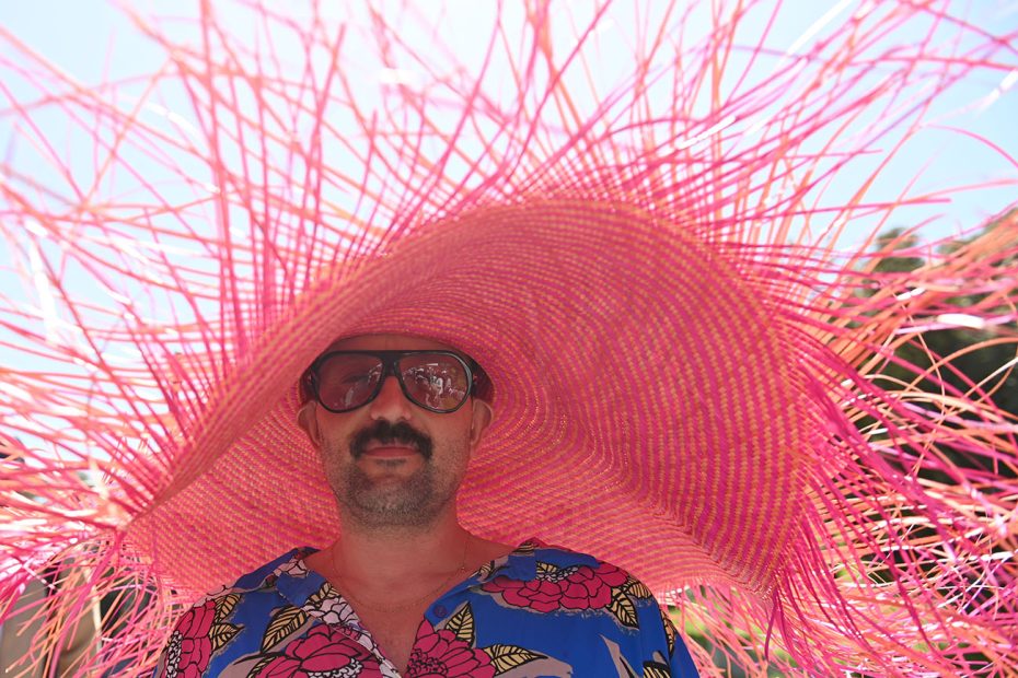 Man wearing sunglasses under a large pink woven sun hat.