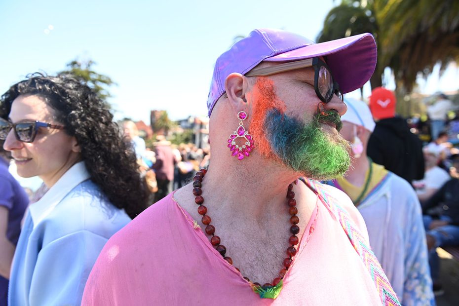 A person with a colorful beard and large earrings enjoying an outdoor event.