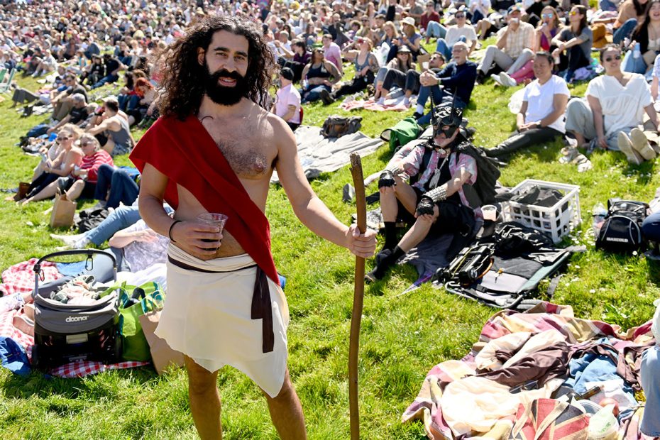 Man dressed in a costume holding a staff standing in a crowded park for Hunky Jesus.