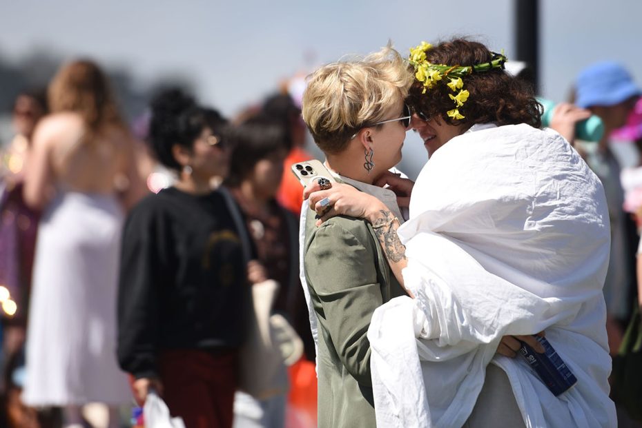 Two people embracing and smiling at each other at an outdoor event with others in the background.