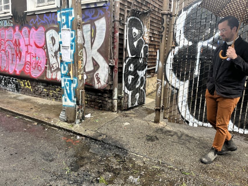 Man walking by graffiti-covered walls while eating and looking at his phone.