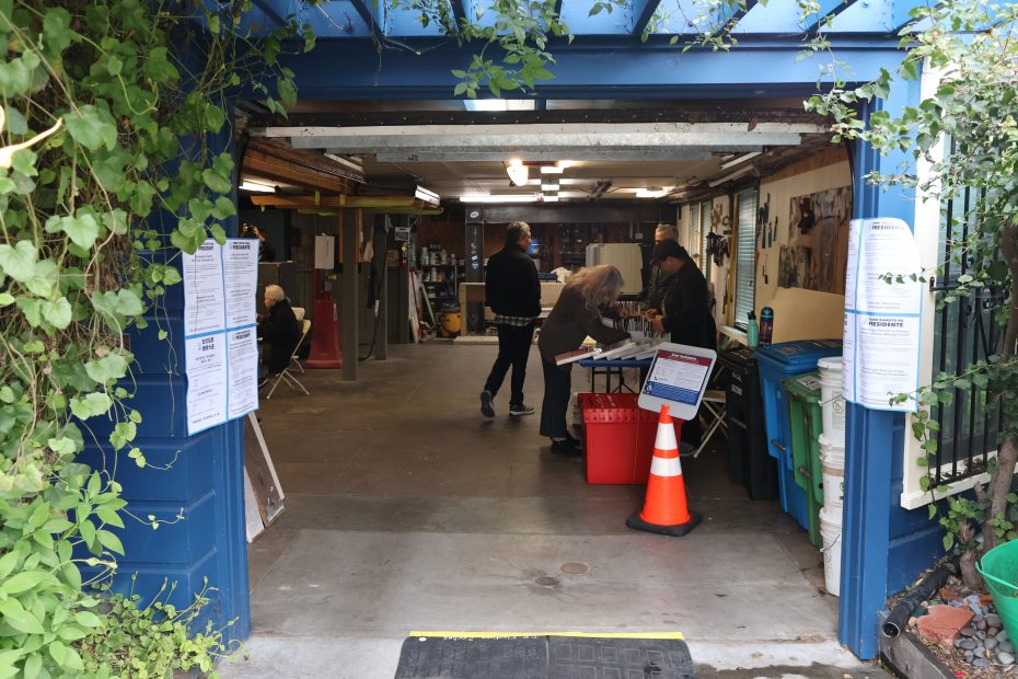 A group of people engaged in activities inside an open garage adorned with green foliage on its entrance.