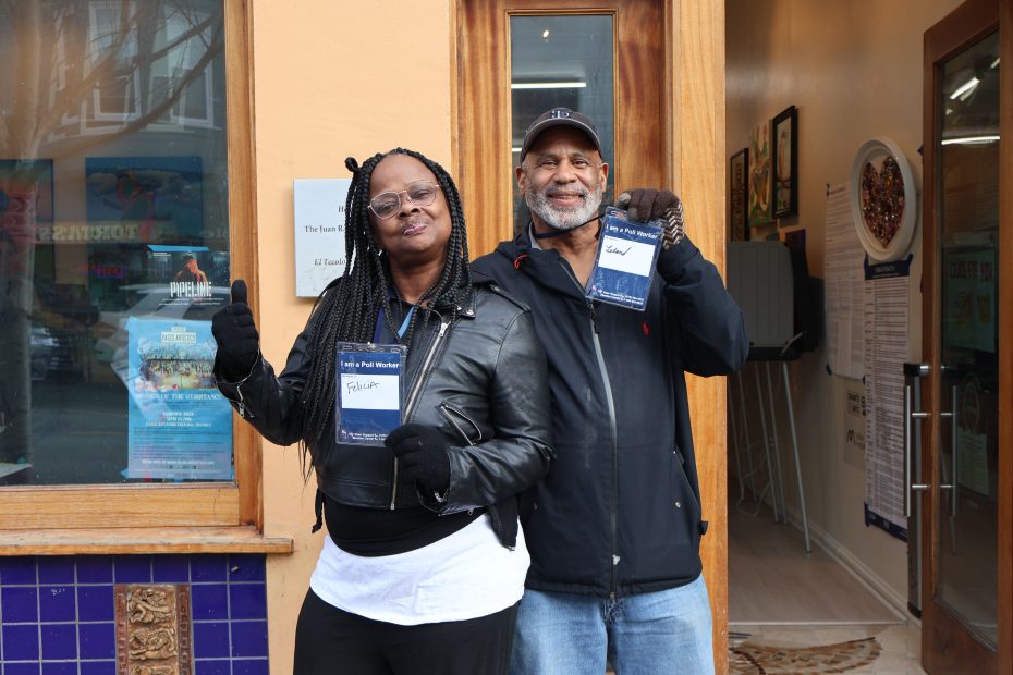 Two poll workers in the Mission standing outside a polling place holding up nametags