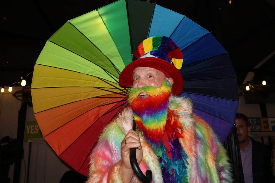 Gaybraham Lincoln, twirling a rainbow colored umbrella, and wearing a rainbow colored bear and coat