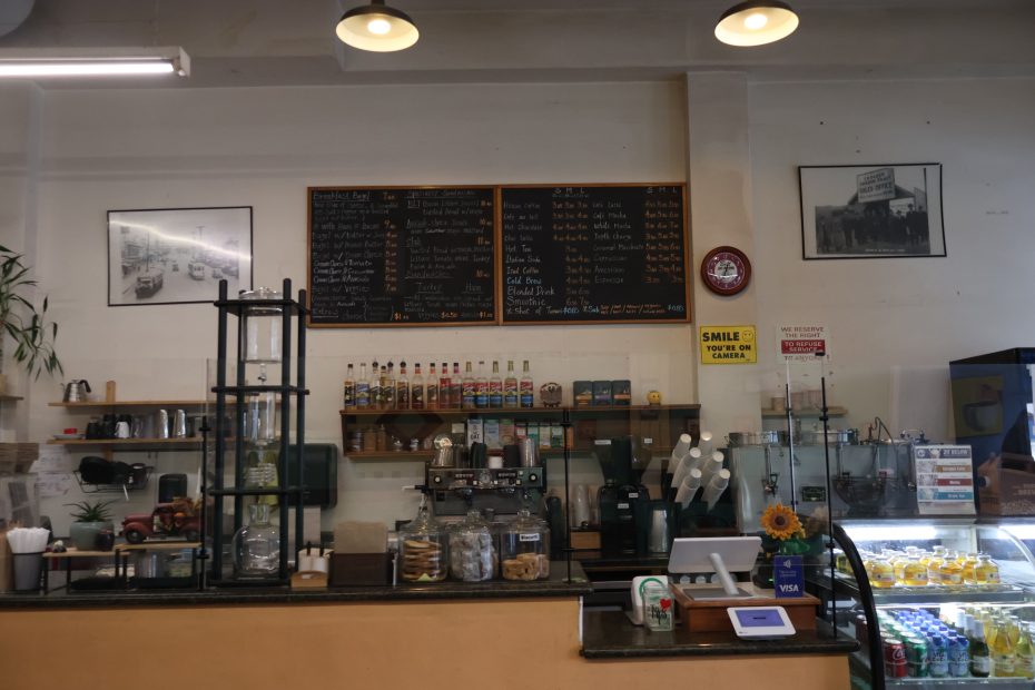 A coffee shop counter with an assortment of pastries on display, Claddagh menu boards above, and a selection of bottled beverages to the right.