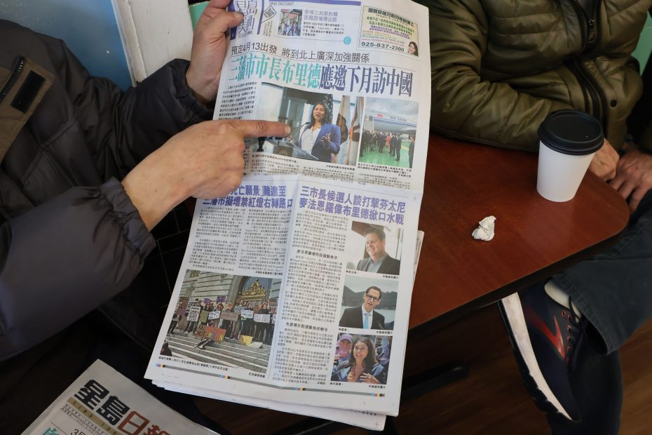 Person reading a Chinese-language newspaper with a Claddagh-design coffee cup on the table.