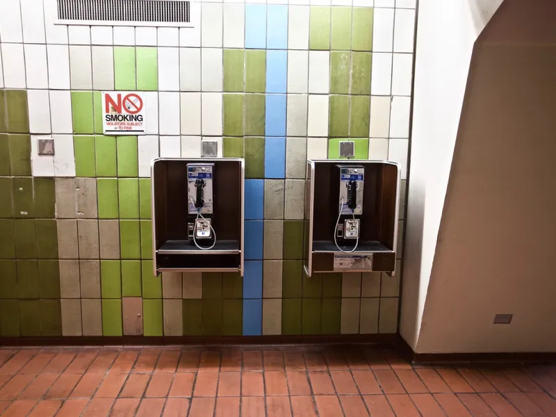 Two payphones mounted on a tiled wall with a "no smoking" sign above.