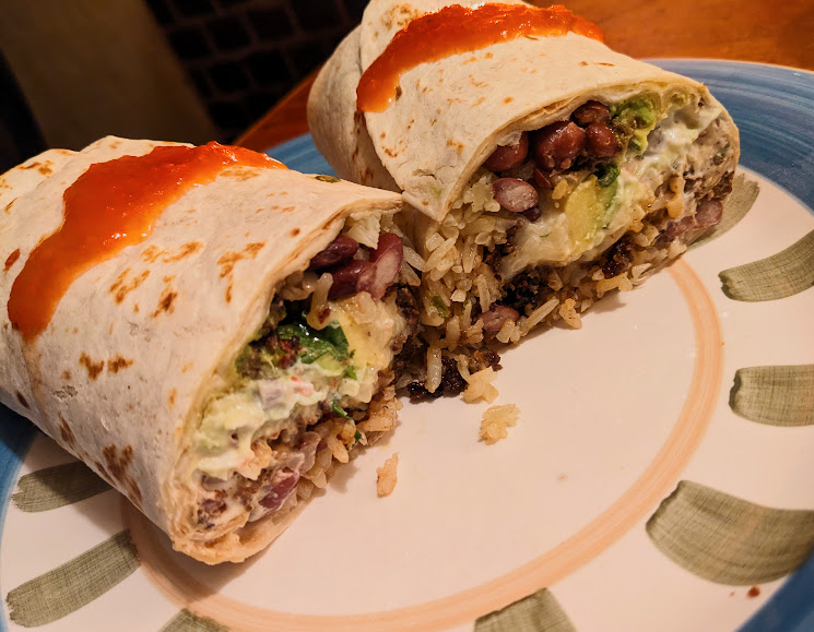 A Sarita's burrito cut in half to reveal its filling of rice, beans, and avocado, served on a plate.