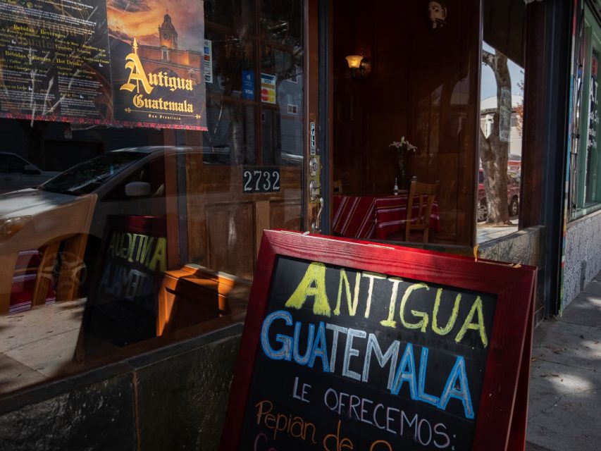 Sidewalk view of a restaurant promoting antigua guatemala cuisine with a chalkboard sign and reflective window.