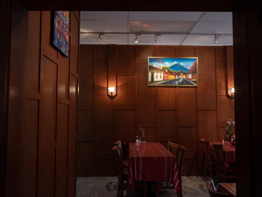 A dimly lit restaurant interior with wooden walls featuring artwork and tables set with red tablecloths.