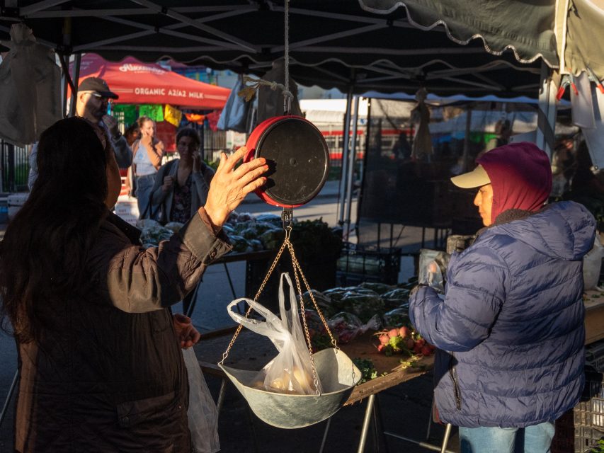 A customer weighs produce at a farmers market stall during the early morning.