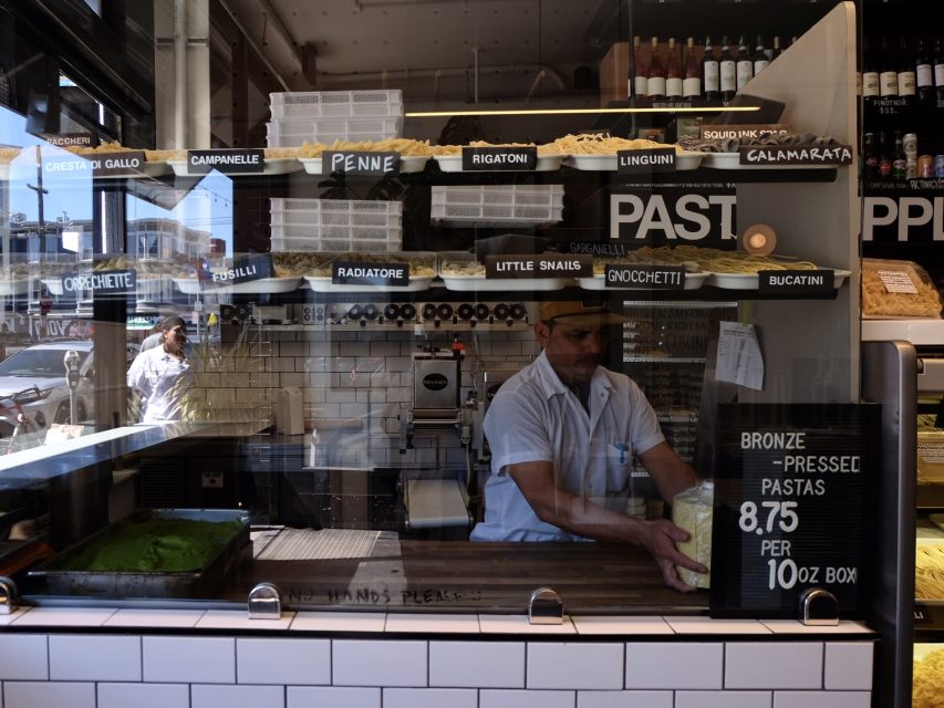 Chef preparing pasta behind a counter in a shop with various types of pasta on display.