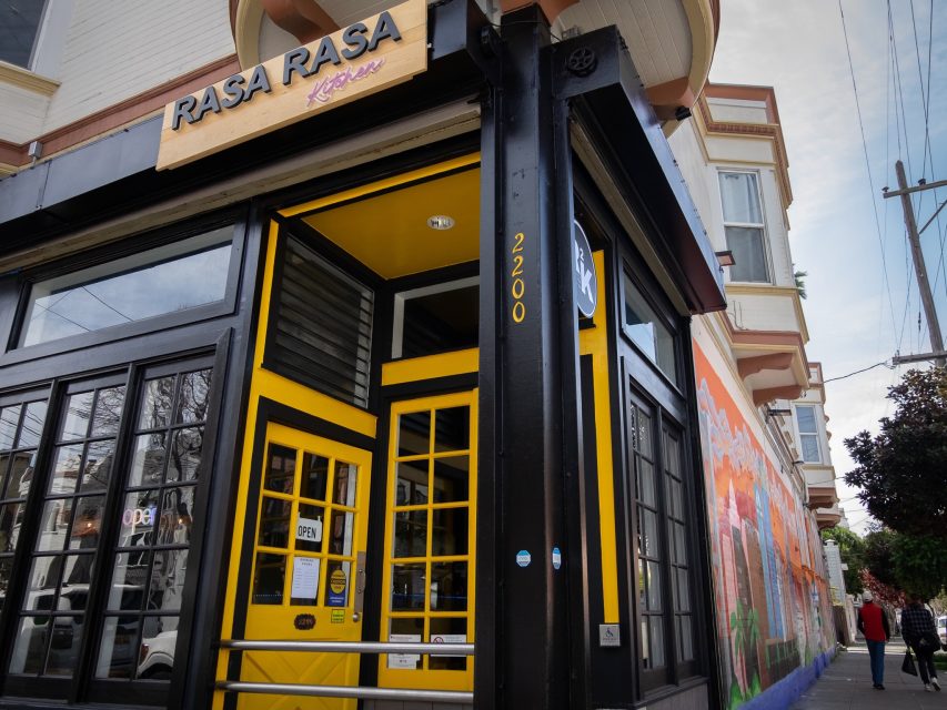 A vibrant yellow and black storefront with the signage "rasa rasa," located on a street corner.