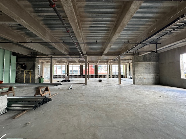 Unfinished interior space of a new commercial building under construction, with exposed ceiling infrastructure and concrete flooring