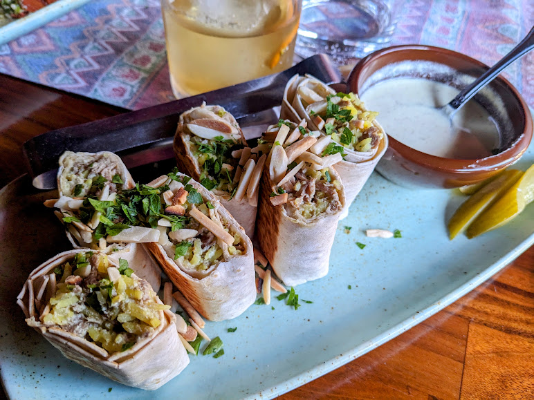 A plate of chicken shawarma wraps accompanied by tahini sauce and a glass of beverage.