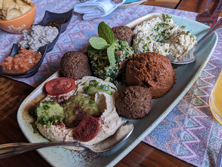 A platter of middle eastern cuisine featuring falafel, hummus, tabbouleh, and various dips, served on a colorful tablecloth.