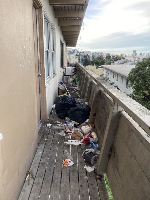 A cluttered balcony with various items and trash strewn across the floor.