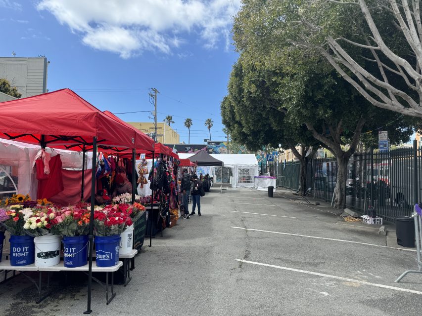 Outdoor market with tents selling goods and flowers under a clear sky.