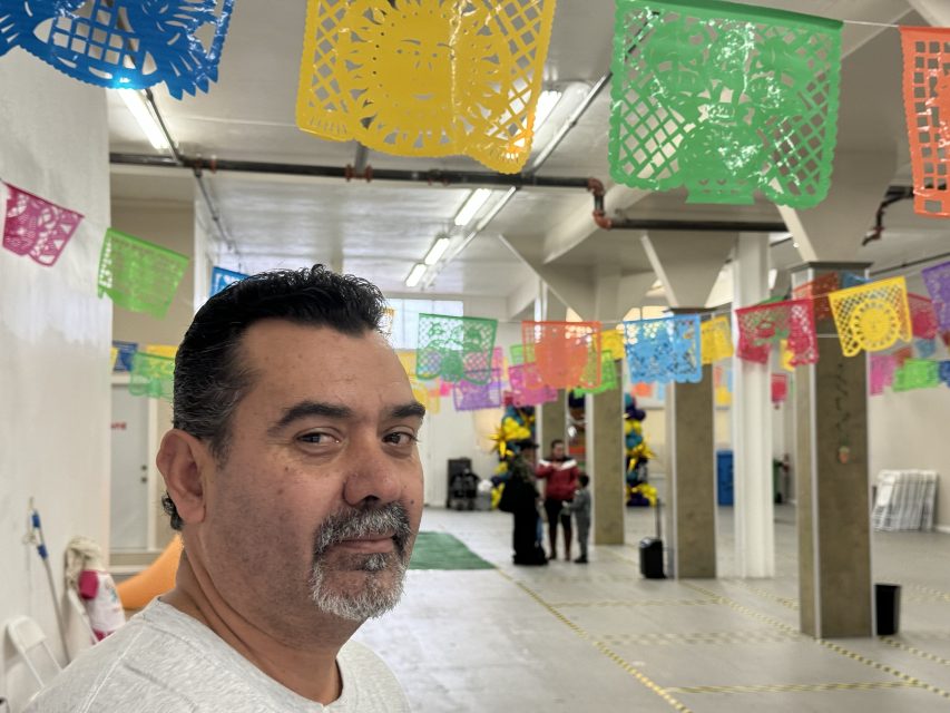 Rodrigo Lopez in a room decorated with colorful papel picado banners.
