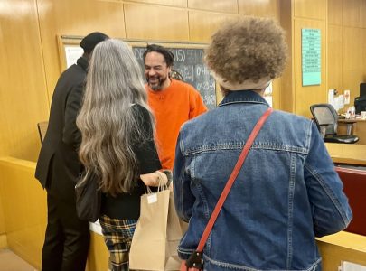 Individuals engaging in a friendly interaction inside a room with a chalkboard menu, under the scrutiny of William Palmer.